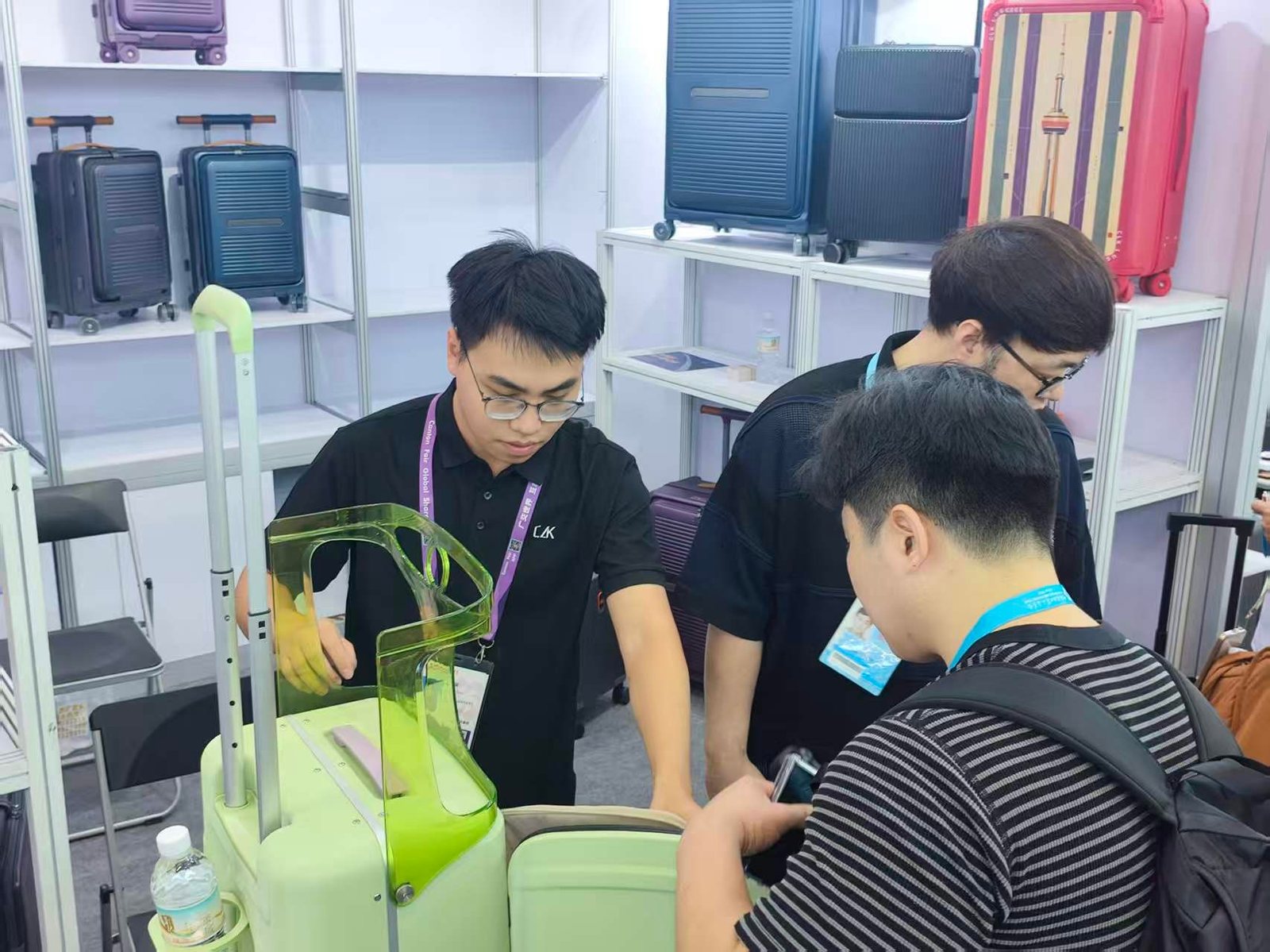 A CLK staff member demonstrating the telescopic handle and lock on a hard-shell case to two buyers